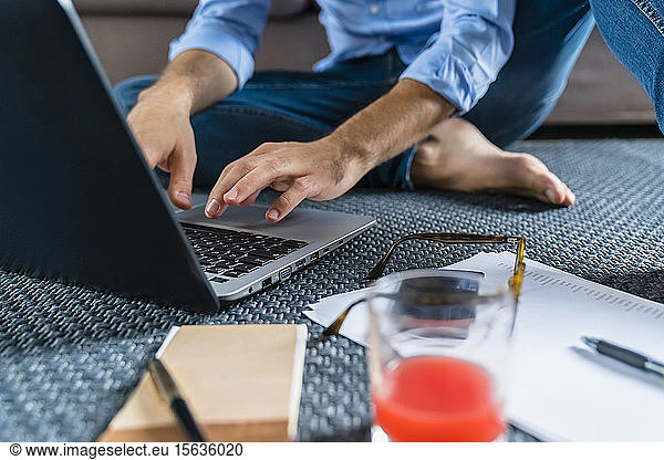 Junger Mann sitzt zu Hause mit Laptop auf dem Boden  Teilansicht