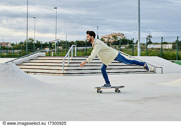 Junger Mann skatet in Freizeitkleidung in einem Skatepark
