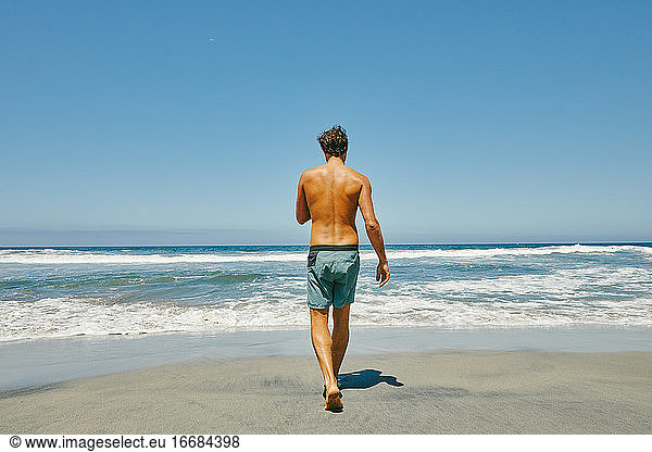 Junger Mann spaziert ohne Hemd zum Pazifik am Strand von Baja  Mexiko.