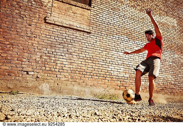 Junger Mann spielt Fußball auf Ödland