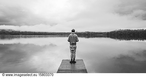 Junger Mann steht auf einem Steg und schaut über einen See  neblige Atmosphäre  Lake Mapourika  Westküste  Südinsel  Neuseeland  Ozeanien