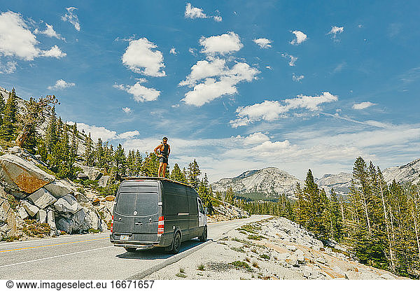 Junger Mann steht auf einem Wohnmobil und betrachtet die Aussicht auf den Yosemite Park.