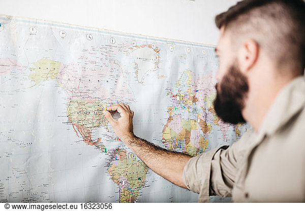 Junger Mann wählt Reiseziele auf einer Weltkarte aus