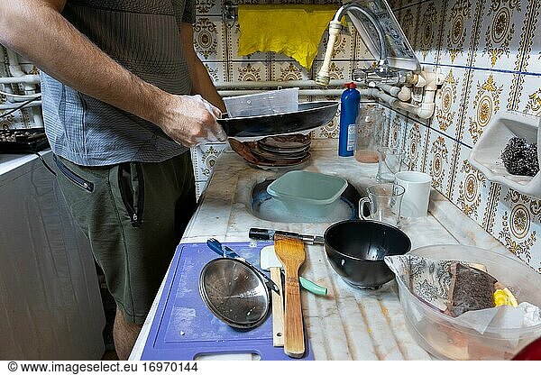 Junger Mann wäscht das schmutzige Geschirr in der unordentlichen Küche.