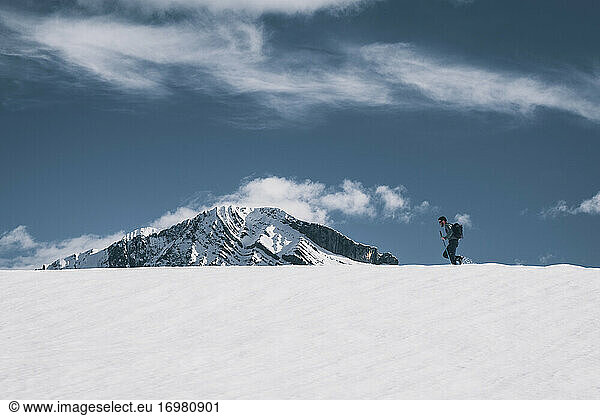 Junger Mann wandert auf einem verschneiten Bergrücken gegen einen schneebedeckten Gipfel