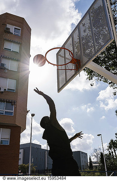 Junger Mann wirft Basketball gegen die Sonne