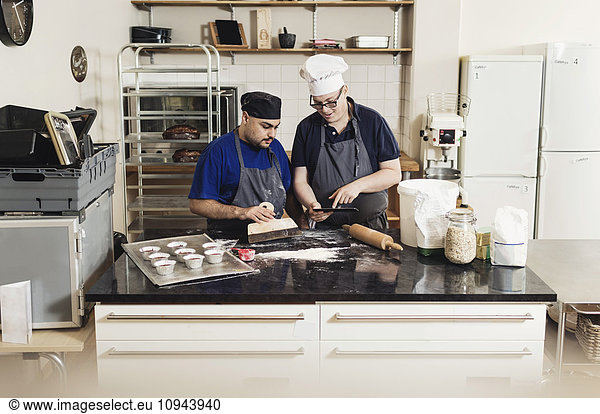 Junger Mann zeigt dem Mitarbeiter beim Kochen in der Küche ein digitales Tablett.