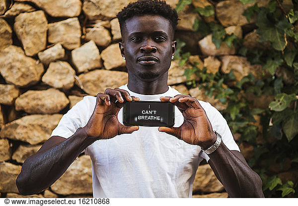 Junger Mann zeigt Text über Smartphone gegen Steinwand