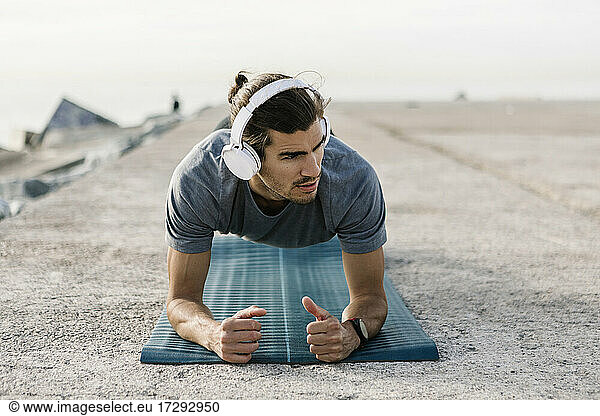 Junger Sportler mit Kopfhörern beim Üben der Plank-Position auf einer Übungsmatte
