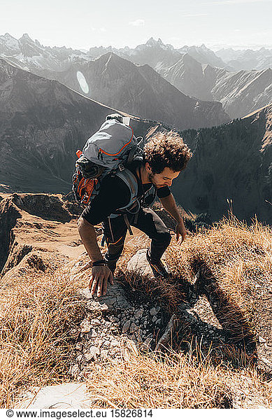 Junger Wanderer klettert steilen Weg vor alpinem Hintergrund