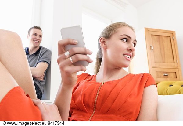 Junges erwachsenes Pärchen im Wohnzimmer mit Handy