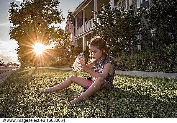 junges Mädchen fängt einen Käfer in einem Glas  das bei Sonnenuntergang im Gras steht