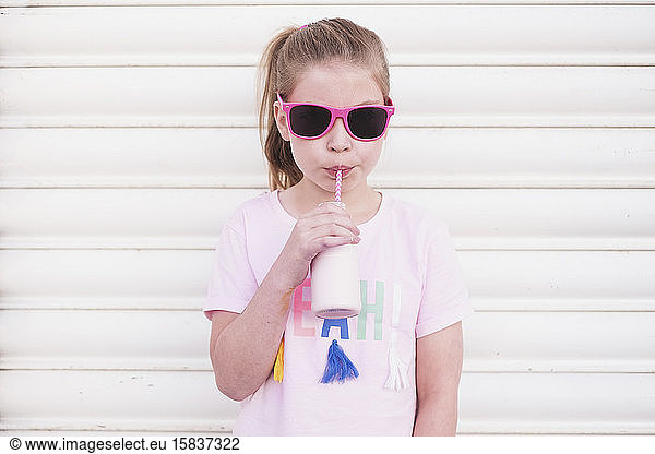 Junges Mädchen mit rosa Sonnenbrille trinkt rosa Milch durch einen Strohhalm
