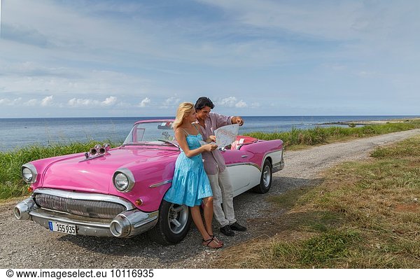 Junges Paar auf der Karte neben Vintage Cabriolet an der Küste  Havanna  Kuba