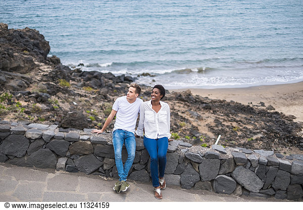 Junges Paar auf Steinmauer an der Küste sitzend