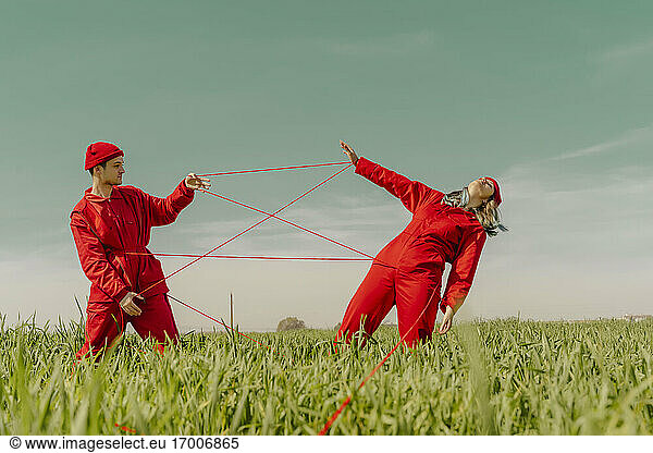 Junges Paar in roten Overalls und Hüten auf einem Feld mit roter Schnur