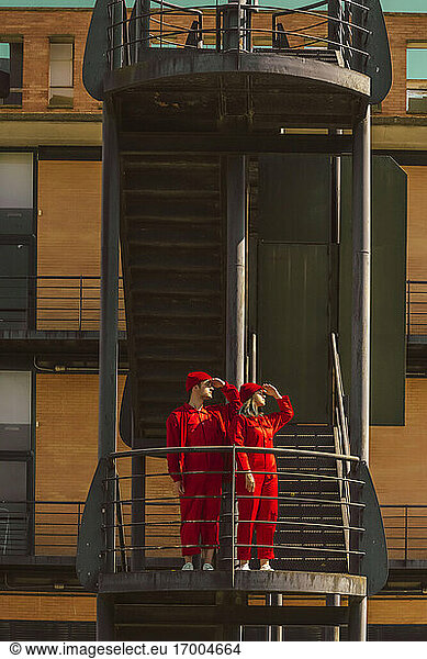 Junges Paar in roten Overalls und Hüten steht auf einem Bahnsteig und schaut in die Ferne