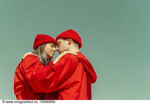 Junges Paar in roten Overalls und Hüten steht Kopf an Kopf gegen den Himmel