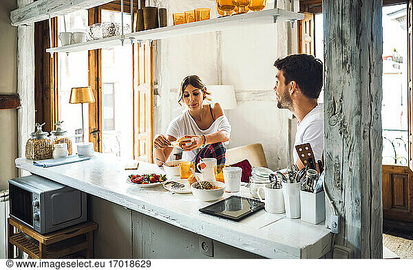 Junges Paar sitzt am Tisch und frühstückt zu Hause