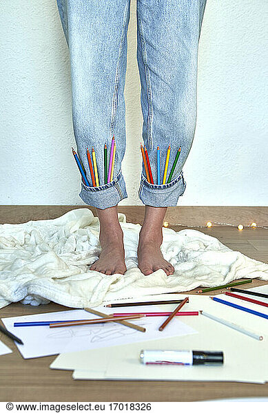 Künstlerin mit Buntstiften in hochgekrempelten Jeans zu Hause