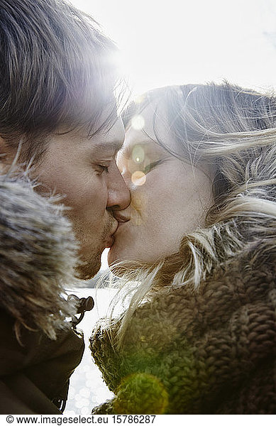 Küssendes junges Paar im Winter bei Gegenlicht