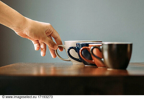 Kaffeetassen in einer Reihe mit einer Hand  die nach ihnen greift