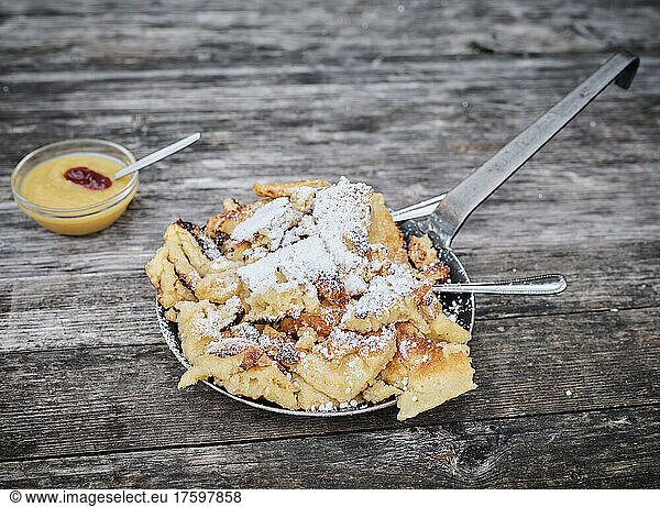 Kaiserschmarren served in cooking pan by apple sauce on wooden table