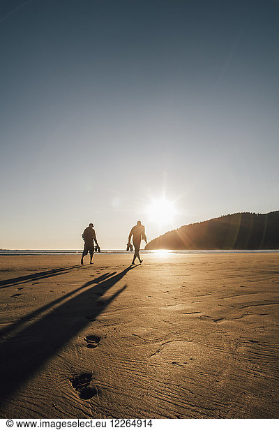 Kanada  British Columbia  Vancouver Island  zwei Männer  die bei Sonnenuntergang am Strand von San Josef Bay spazieren gehen.