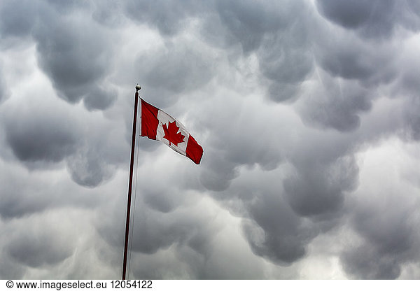 Kanada-Flagge am Mast gegen eine dramatische Sturmwolkenformation; Calgary  Alberta  Kanada