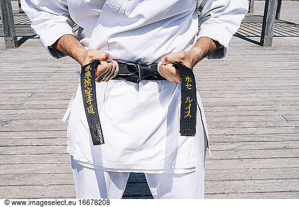 Karate man tying the knot of his black belt