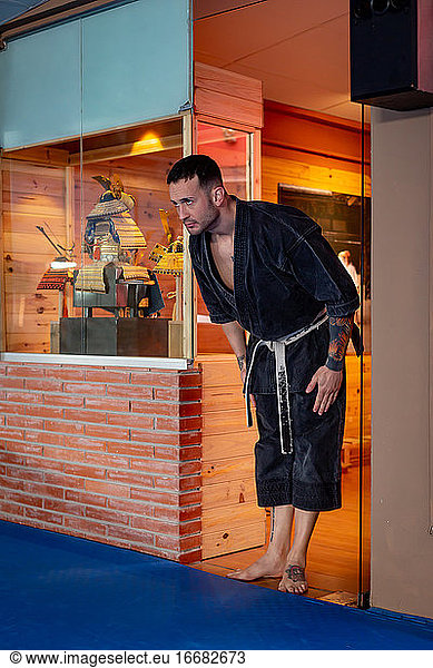 Karate-Mann posiert mit einer Verbeugung für den Zugang auf Tatami und trägt einen schwarzen Kimono