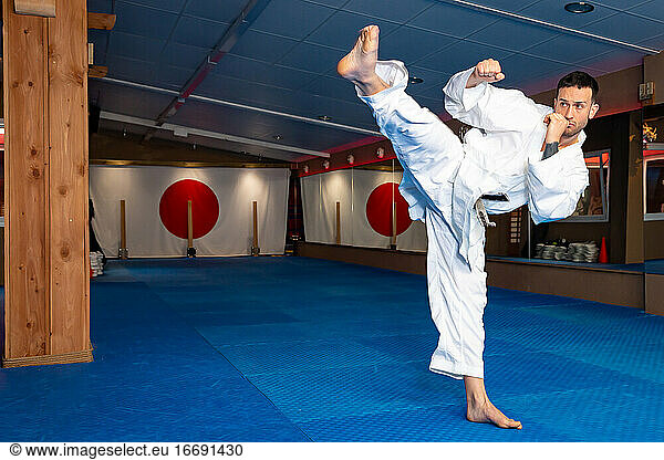 Karate-Mann steht auf Tatami und trägt einen weißen Kimono in Aktion