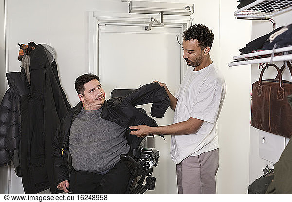 Karriere hilft Mann im Rollstuhl beim Anziehen der Jacke