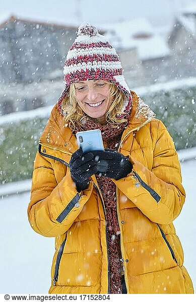 Kaukasische junge Frau genießt mit einem Mobiltelefon im Schnee im Freien im Winter Zeit. Navarra  Spanien  Europa.