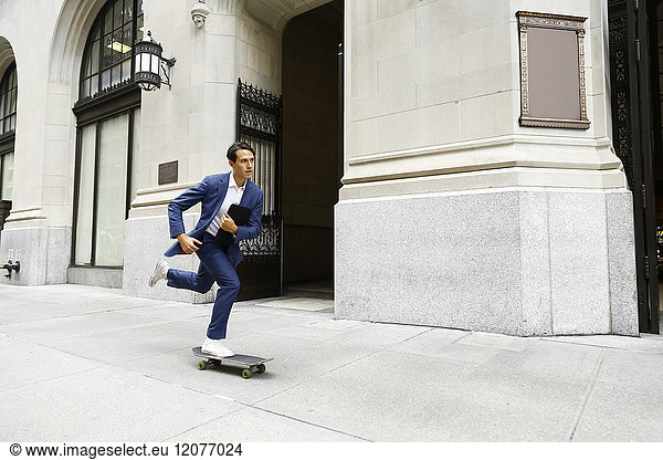Kaukasischer Geschäftsmann der auf einem städtischen Bürgersteig Skateboard fährt