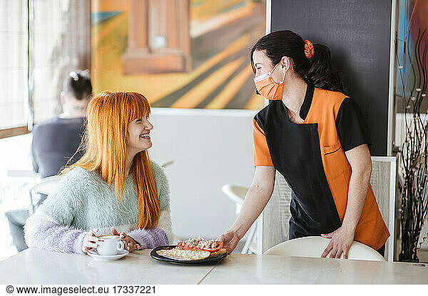 Kellnerin serviert einer Kundin in der Cafeteria ein Sandwich