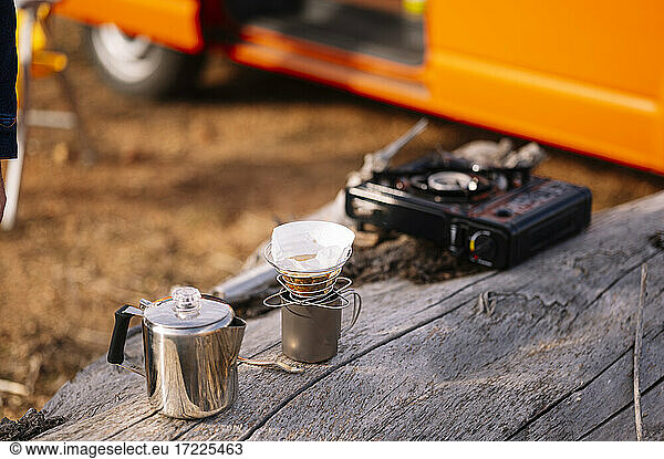 Kettle with coffee mug and camping stove on wooden log