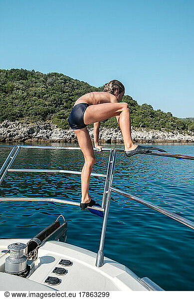 Kid diving from yacht in the sea wearing flippers.