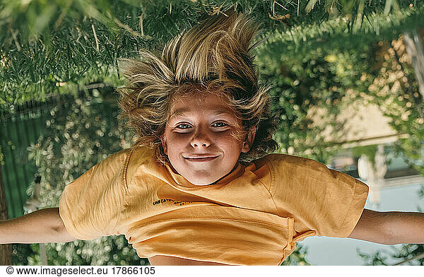 Kid hanging upside down while playing outdoors at backyard.