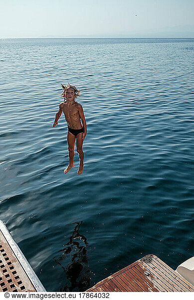 Kid in mid air while diving into the sea from yacht.