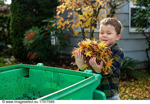 Kid putting pile of leaves into yard waste bin