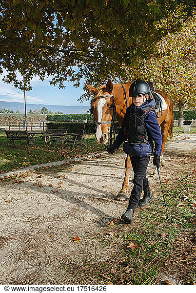 Kid walking with horse at ranch after riding.