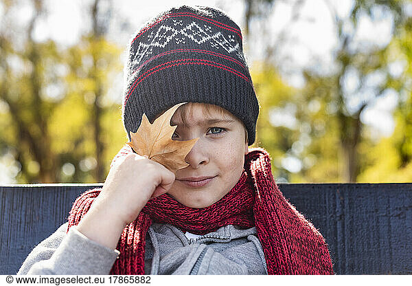 Kid with a leave in his hand  wearing a woolen Hat and scarf. Fall