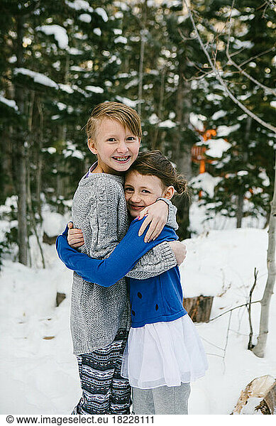 Kids hug in snow covered forest in sweaters and warm clothes