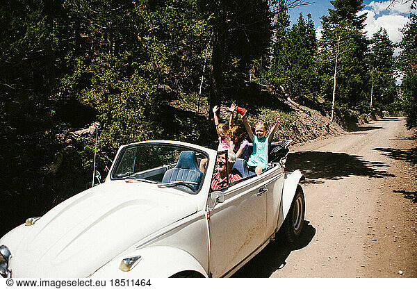 Kids in an old car with grandpa driving in green forest on dirt road