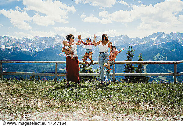 Kids jumping with two moms in mountains on sunny day