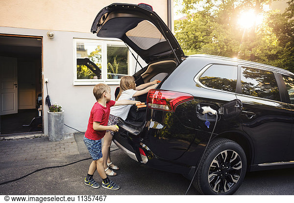 Kids loading black electric car trunk against house in back yard