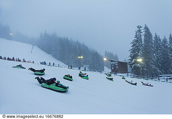Kids slide down a hill on a tube at night at a ski resort in Oregon.