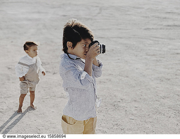 Kind fotografiert mit einer Oldtimer-Kamera  während ein anderes Kind im Hintergrund steht