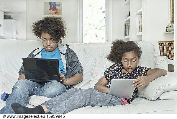 Kinder  die Laptop-Computer benutzen und auf einem Sofa sitzen.